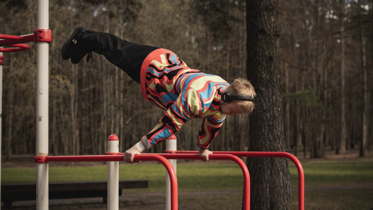 Young man wearing colorful outfit doing calisthenics on red bars in Vilnius park.